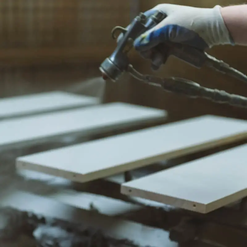 Close-up of a gloved hand painting a bed with a spray gun