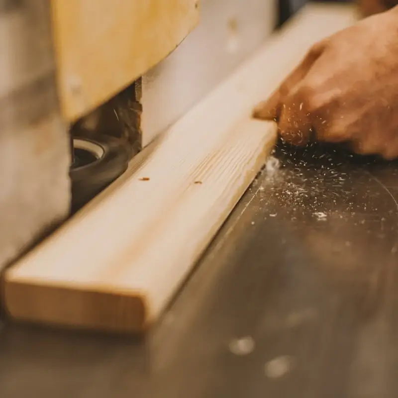 Close-up of a person’s hand cutting a wooden board with a stationary carpentry machine