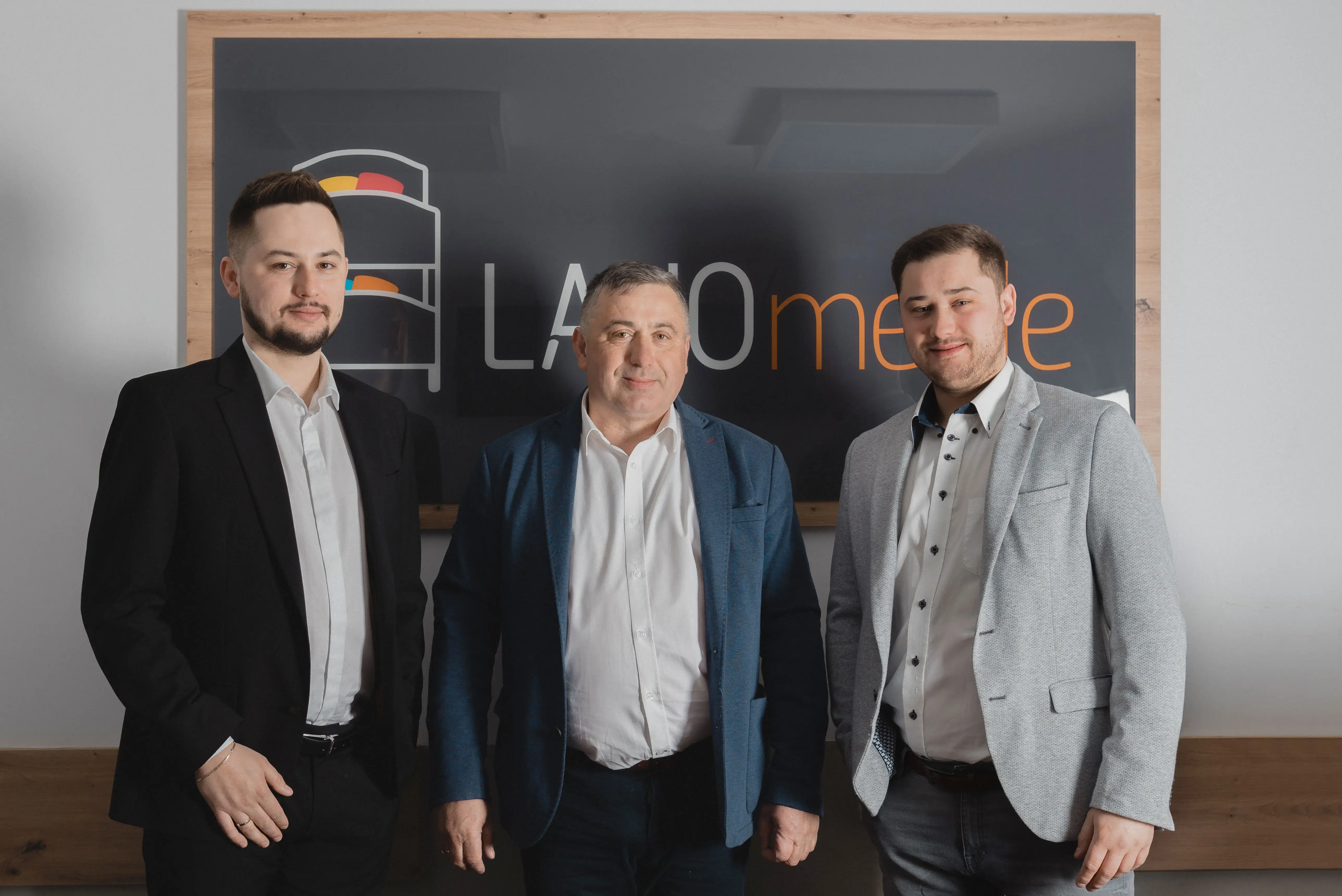 The founders of LANO – a father with his two sons, smiling in suits in front of a panel with the LANO logo