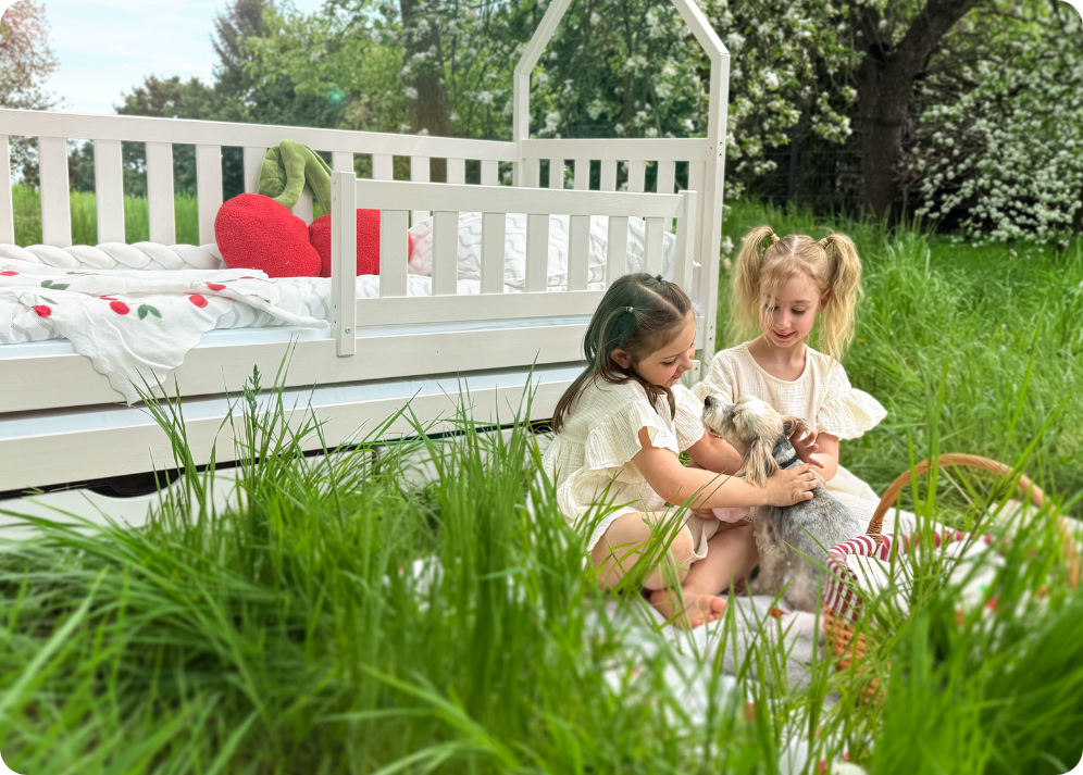 Two girls sitting in a clearing in front of a cotton bed, petting a small dog
